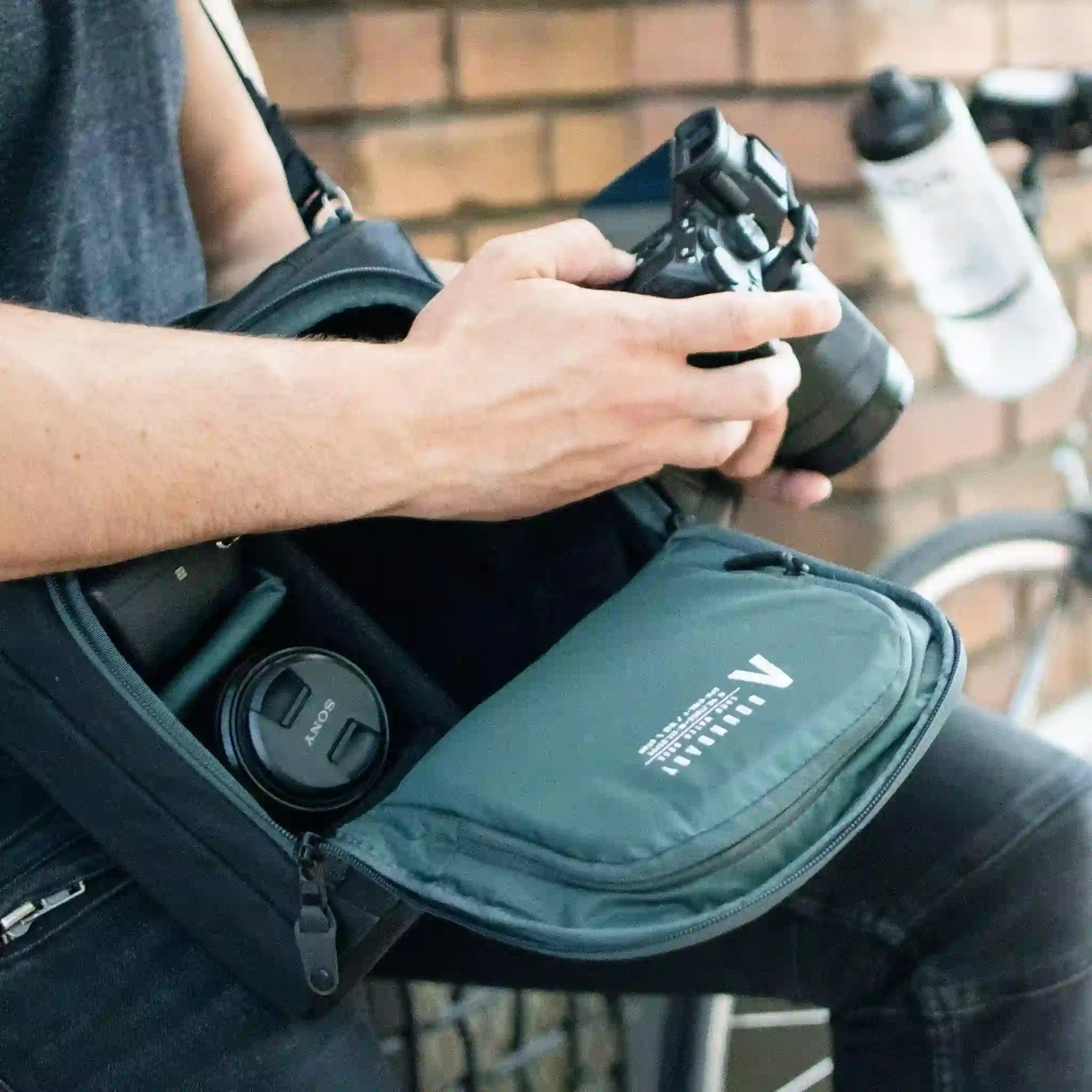 A man with a Camera Cube strapped over his shoulders, as he adjusts the settings on his camera.